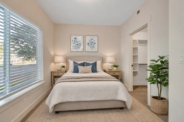 Bright and inviting bedroom with plush bedding, serene decor, and ample natural light from a large window, featuring modern side tables and a walk-in closet.