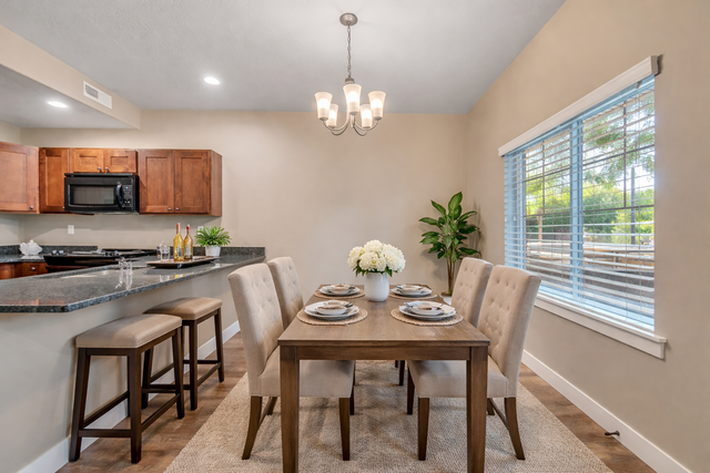 Elegant dining area with a wooden table set for six, complemented by plush upholstered chairs. The open kitchen features a sleek countertop and warm wooden cabinets, creating an inviting space for gatherings.