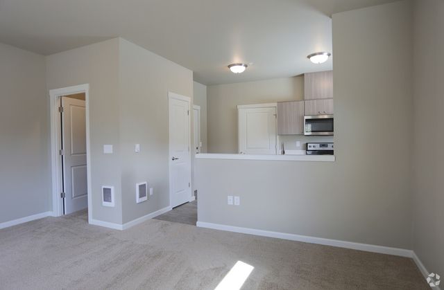 Open-concept living area with modern kitchen and cozy beige carpeting, featuring sleek appliances and bright lighting.