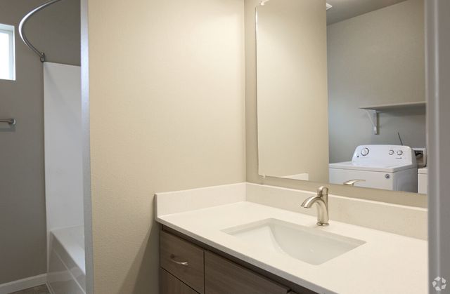 Modern bathroom with sleek countertop and spacious laundry area featuring a washer and dryer for convenient living.