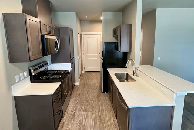 Modern kitchen with sleek dark cabinetry, stainless steel appliances, and elegant marble countertops leading to an open doorway.