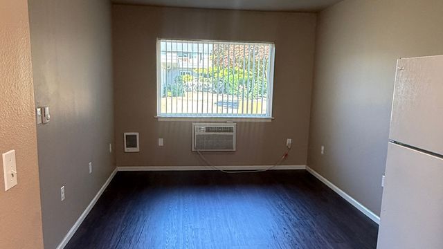 Bright room with large window, air conditioning unit, and dark hardwood floors, offering a cozy and inviting atmosphere.