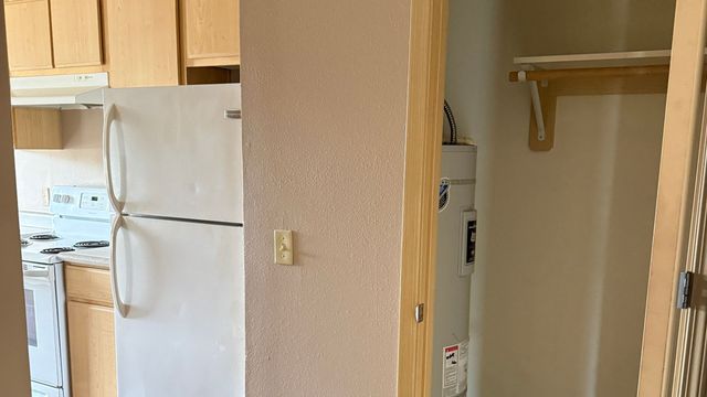 Cozy kitchen space with a classic white refrigerator, electric stove, and wooden cabinets, adjacent to a compact utility closet.