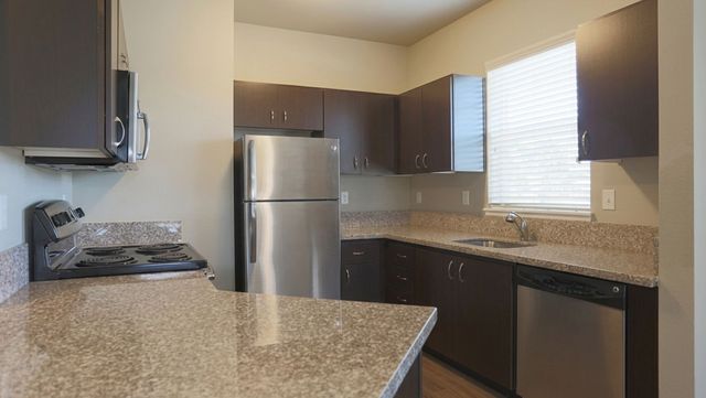 Modern kitchen with sleek dark cabinets, stainless steel appliances, and granite countertops, offering abundant natural light.