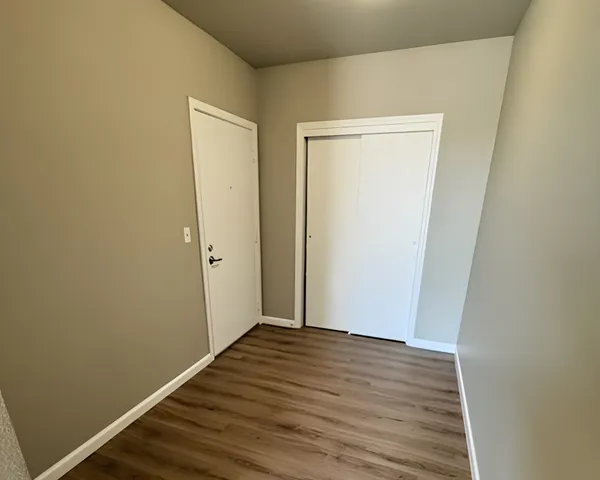 Modern entryway featuring sleek hardwood floors, neutral walls, and ample closet space with white sliding doors.