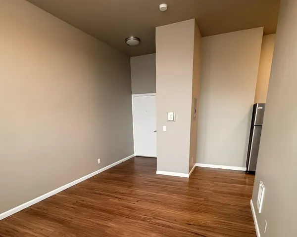 Modern apartment entryway with elegant hardwood flooring and high ceiling, featuring a sleek stainless steel refrigerator tucked into the corner.