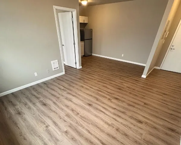 Contemporary apartment interior showcasing sleek wood flooring, neutral walls, and a cozy kitchenette area.