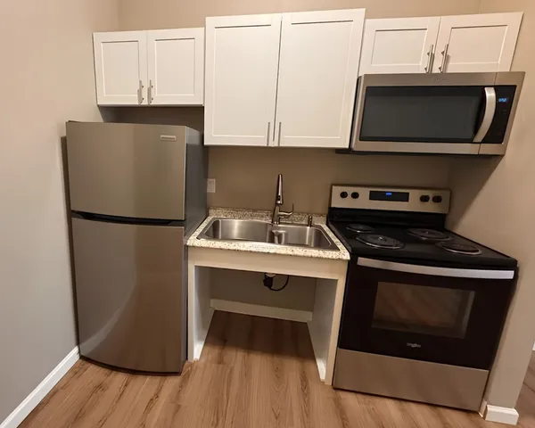 Modern compact kitchen with sleek stainless steel appliances, granite countertops, and elegant white cabinetry in a cozy apartment setting.