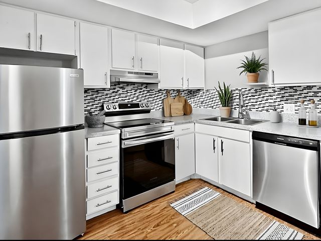 Modern kitchen with sleek stainless steel appliances, white cabinetry, and stylish backsplash, complemented by wooden flooring and potted plants for a fresh ambiance.