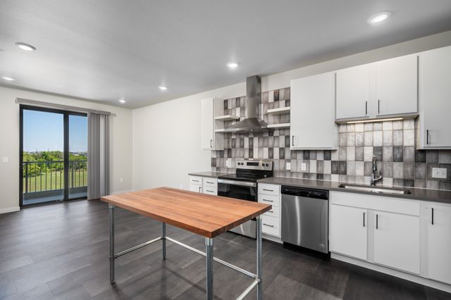 Modern kitchen featuring sleek cabinetry, stainless steel appliances, and a large wooden island, with a scenic view through sliding glass doors.