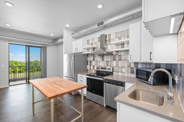 Modern kitchen with stainless steel appliances, spacious wooden island, and scenic balcony view enhancing natural light.