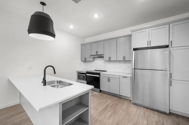 Modern kitchen with sleek grey cabinets, stainless steel appliances, and an elegant pendant light over a spacious white island.