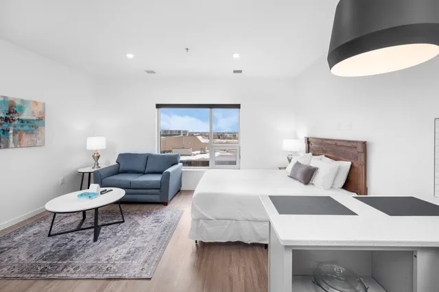 Modern studio apartment with stylish decor featuring a cozy bed, chic sofa, and contemporary artwork. Ample natural light floods the space, highlighting a sleek kitchenette and elegant furnishings.