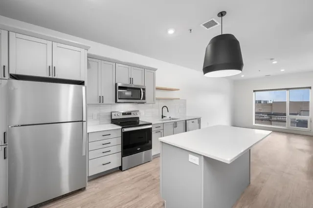 Contemporary kitchen featuring sleek gray cabinetry, stainless steel appliances, and a spacious island under modern lighting.