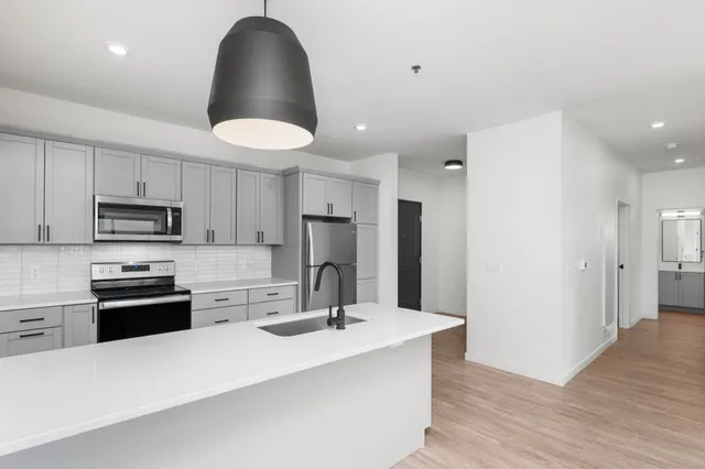 Modern kitchen with sleek gray cabinets, stainless steel appliances, and a spacious island with a stylish black pendant light.