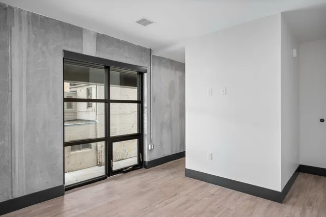 Modern industrial-style apartment with concrete walls, a large window, and sleek wooden flooring.