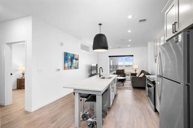Modern open-concept kitchen and living room with sleek finishes, featuring a cozy sofa, vibrant artwork, and large window with city view.