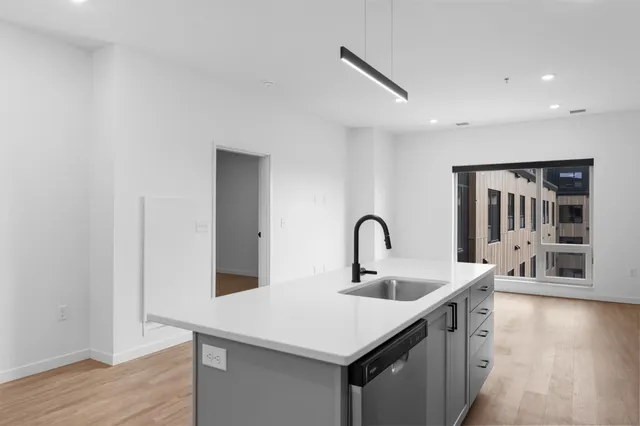 Modern apartment kitchen with sleek island, stylish faucet, bright wood floors, and large window offering ample natural light.