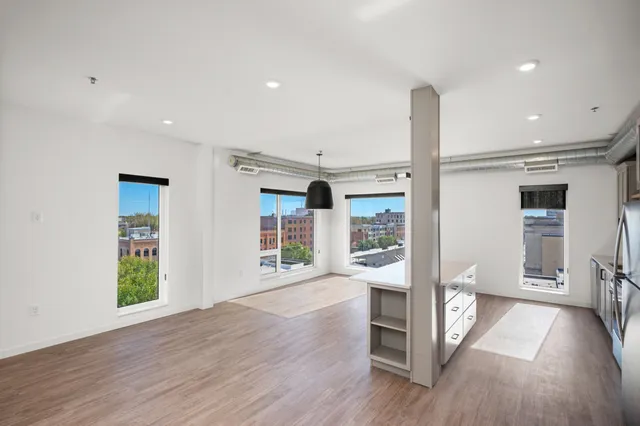 Bright and spacious modern apartment with open-concept design, large windows offering city views, and sleek wooden flooring.