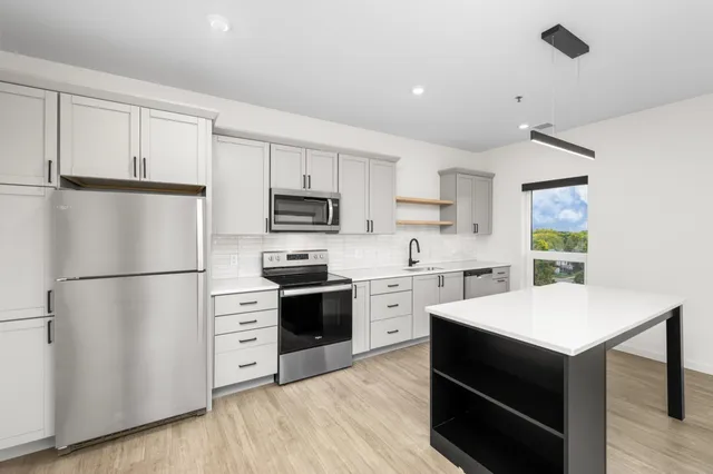 Modern kitchen with sleek gray cabinets, stainless steel appliances, and a spacious island under stylish lighting.