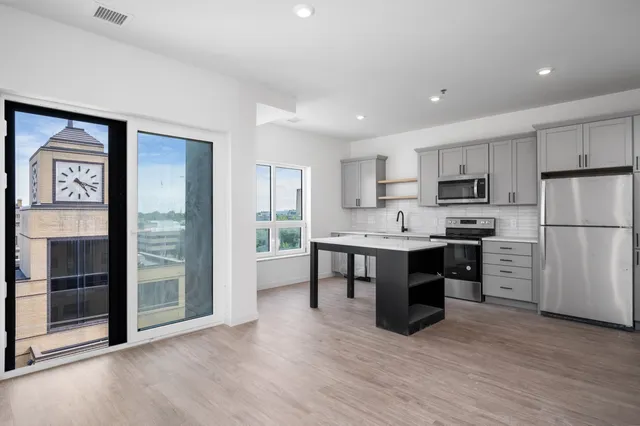 Modern open-concept kitchen with sleek gray cabinets, stainless steel appliances, and wood flooring, featuring a picturesque window view of a clock tower.