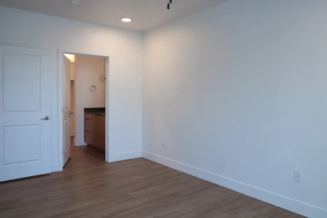 Modern bedroom with sleek wooden flooring and an open doorway leading to a chic bathroom area.