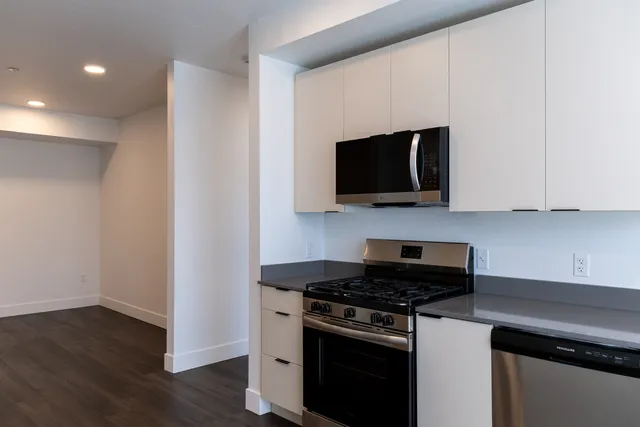 Modern kitchen with sleek white cabinets, stainless steel appliances, and elegant dark wood flooring, offering a spacious and functional cooking environment.
