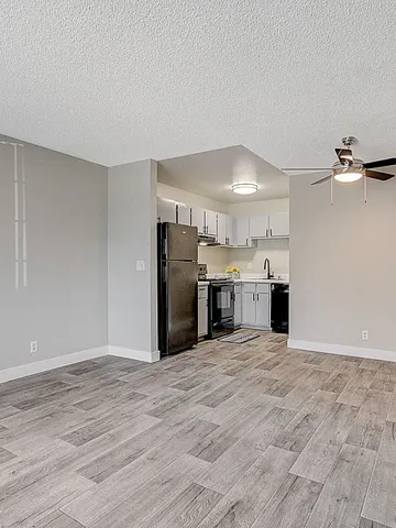 Modern apartment interior with open-concept kitchen and living area, featuring sleek gray flooring and ceiling fan.