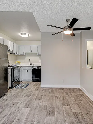 Sleek modern kitchen with black appliances and open floor space, featuring light wood flooring and a ceiling fan.