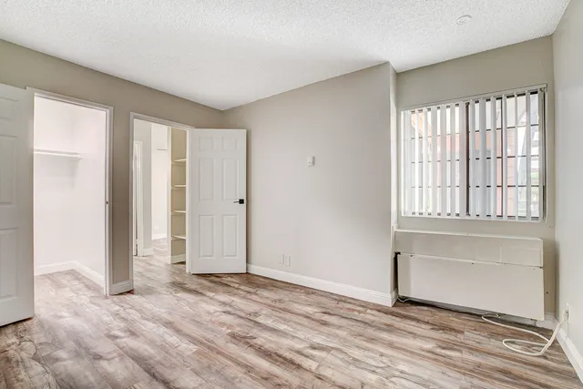 Spacious bedroom with elegant wood flooring, large window with blinds, and open closet doors.