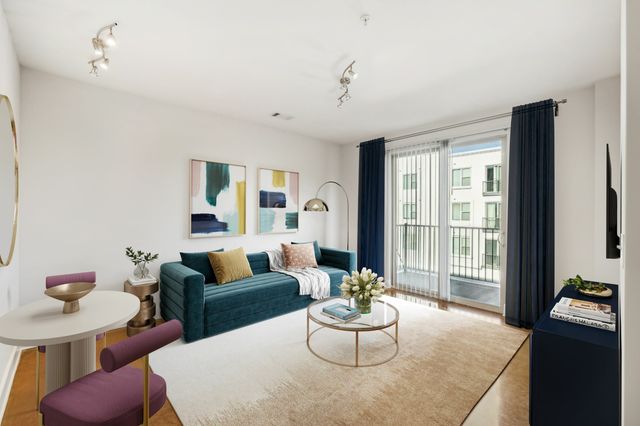 Chic 1-bedroom apartment living room featuring a teal velvet sofa, modern art, and a glass coffee table with elegant decor, adjacent to large windows with stylish curtains at The Melrose in Nashville