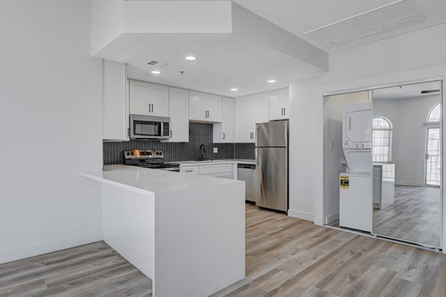 Modern kitchen with sleek white cabinetry, stainless steel appliances, and stylish herringbone backsplash.
