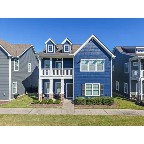 Charming two-story blue house with white accents, featuring dormer windows, a welcoming porch, and well-maintained landscaping in a serene neighborhood setting.