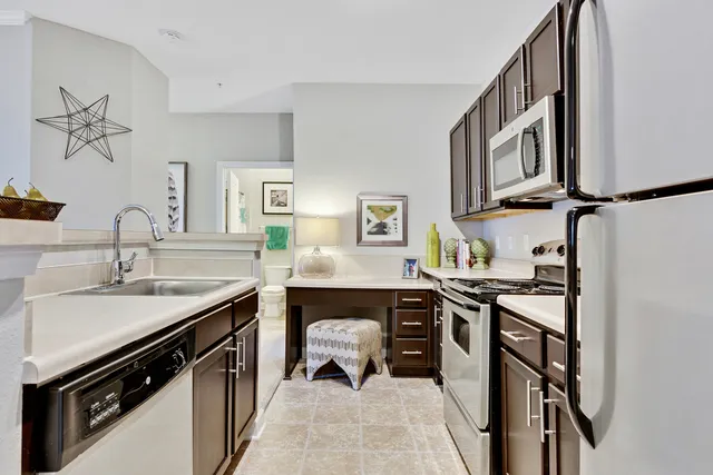 Modern kitchen with stainless steel appliances, sleek dark wood cabinets, and a cozy workspace with plush seating.
