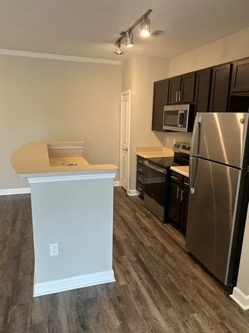 Modern kitchen with sleek stainless steel appliances, dark cabinetry, and polished wooden flooring under stylish track lighting.