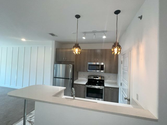 Modern kitchen with stainless steel appliances, elegant pendant lighting, and a cozy breakfast bar, perfect for culinary enthusiasts.
