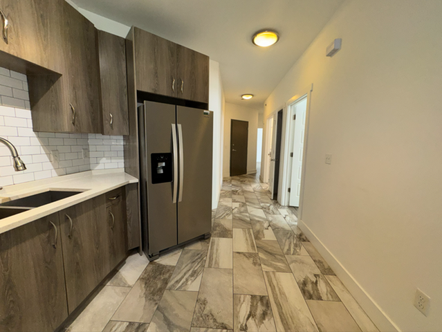 Modern kitchen featuring sleek stainless steel appliances, elegant wood cabinetry, and stunning tile flooring with a bright and inviting hallway view.