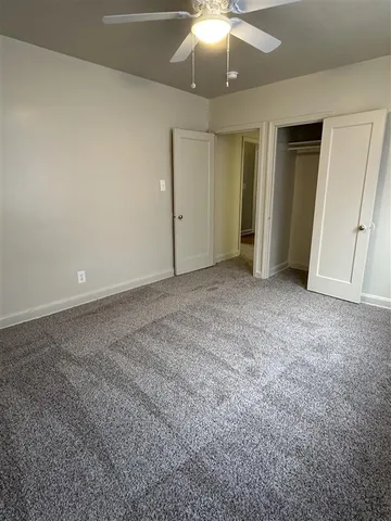 Inviting bedroom with plush carpet, ceiling fan, and spacious closet, perfect for a cozy and functional living space.