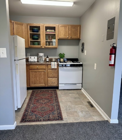 Charming kitchenette with wooden cabinets, a compact stove, refrigerator, and cozy decor for a welcoming touch.