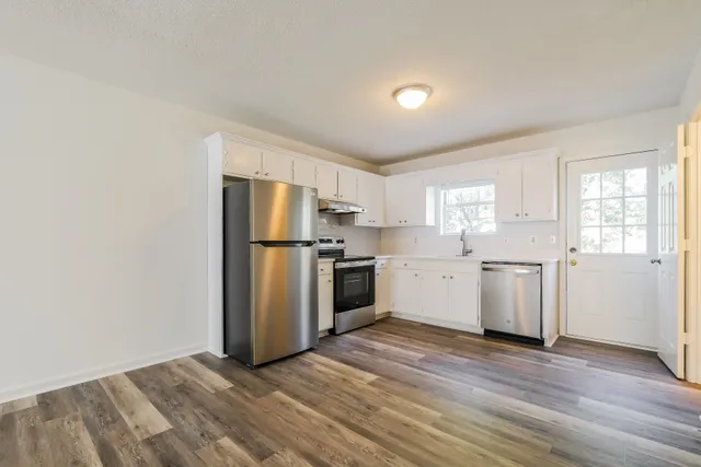 Modern kitchen with stainless steel appliances, white cabinetry, and elegant wood flooring, brightened by natural light from a window.