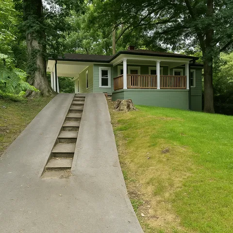Charming green home with inviting front porch nestled among lush trees, featuring a unique elevated pathway.