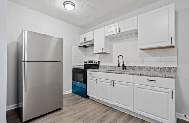 Modern kitchen with granite countertops, sleek stainless steel refrigerator, and stylish white cabinetry, perfect for contemporary living.