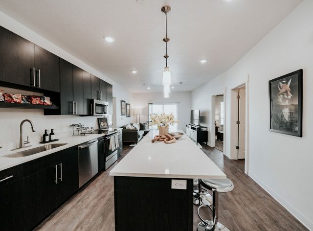 Modern open-concept kitchen with sleek dark cabinets, elegant lighting, and spacious island leading into a cozy living area, perfect for entertaining.