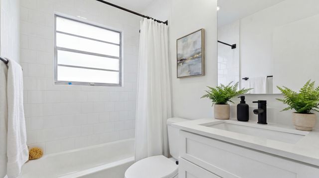Bright, modern bathroom with elegant white tiles, contemporary artwork, and lush green plants.