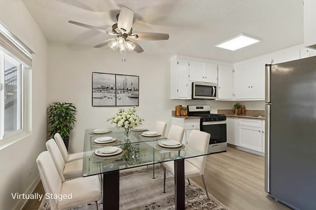 Elegant, virtually staged kitchen and dining area featuring a sleek glass table set for six, modern stainless steel appliances, and bright white cabinetry, creating a welcoming and stylish atmosphere.