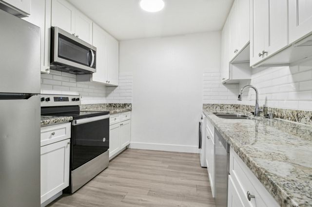 Modern kitchen with sleek stainless steel appliances, granite countertops, white cabinetry, and stylish wood flooring.