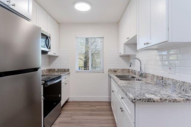 Bright, modern kitchen with granite countertops, white cabinets, stainless steel appliances, and wood flooring.