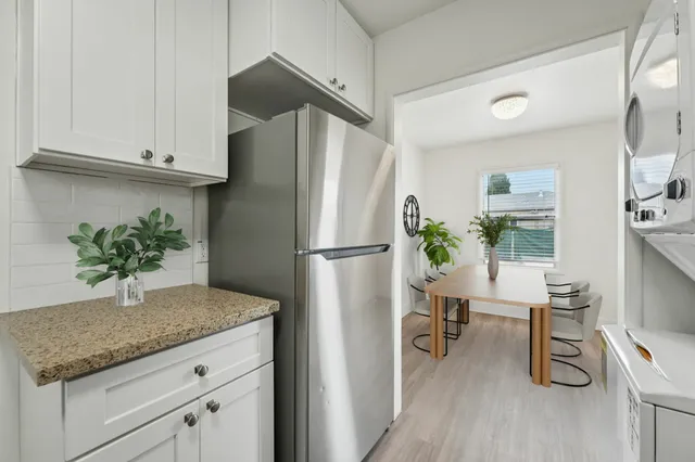 Modern kitchen view featuring a stainless steel refrigerator, white cabinetry, and an adjoining dining area with natural light and contemporary decor.