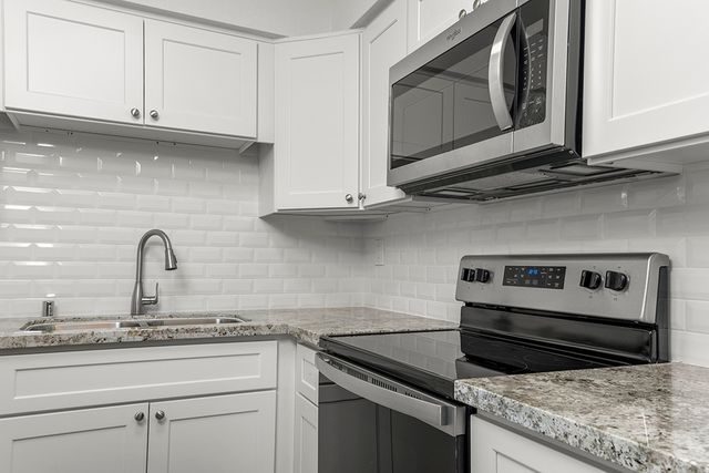 Modern kitchen with sleek stainless steel appliances, granite countertops, and elegant white cabinetry accentuated by a glossy subway tile backsplash.