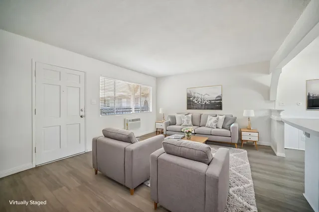Bright and inviting living room with chic gray sofas, large window, modern artwork, and light wooden flooring.